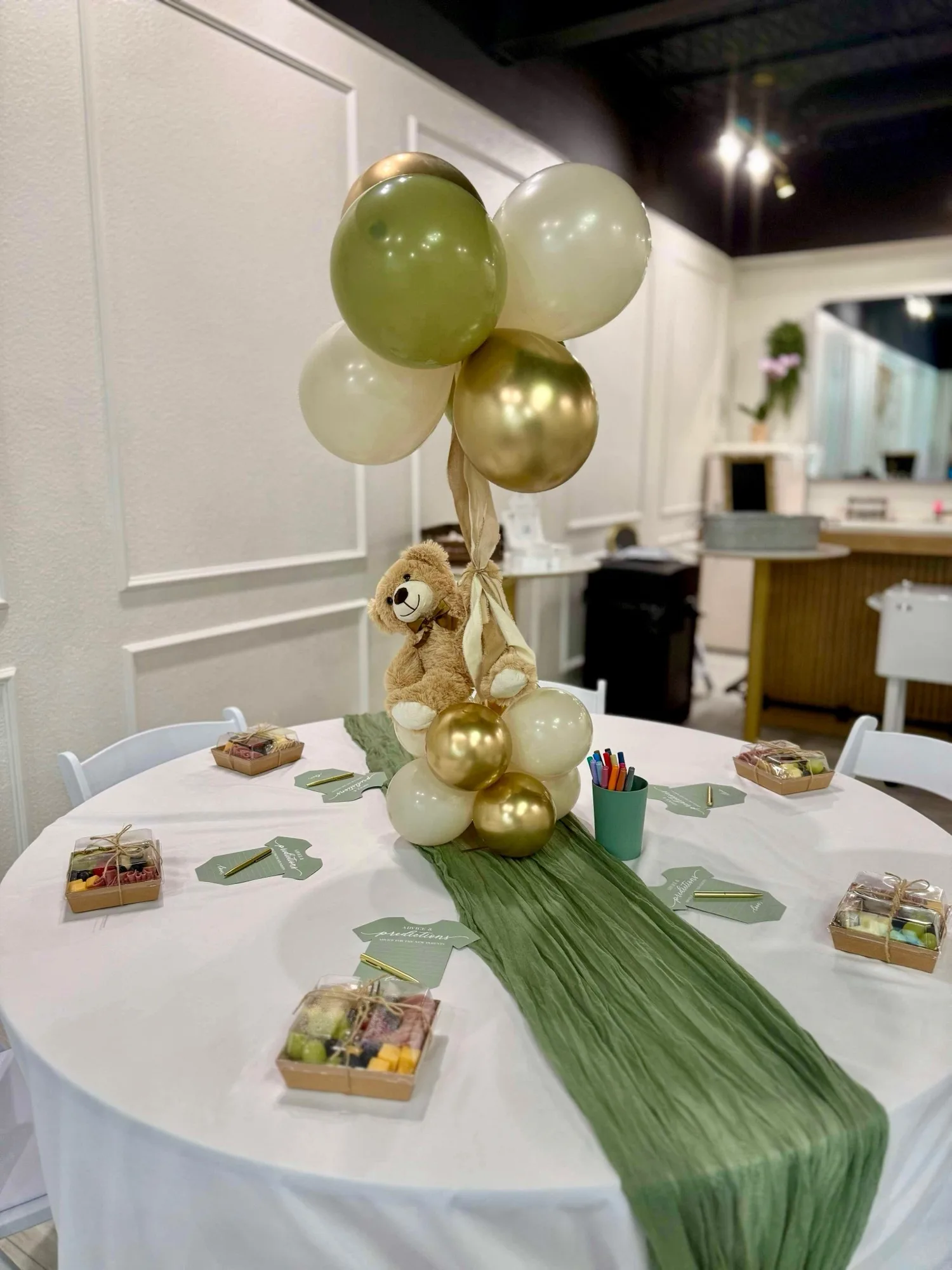 Baby shower table with teddy bear centerpiece and green and gold balloons at Aramas Events